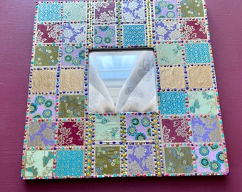 May include: Square decorative mirror with a mosaic-like design. The frame is composed of small, patterned squares in shades of purple, green, gold, and blue. The edges are adorned with small, colorful beads. The mirror has a square reflective surface.