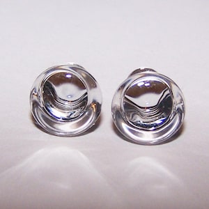 May include: Two clear, glass cabinet knobs with a rounded, concave design. The knobs are transparent, reflecting light and creating a bright, clean aesthetic. The knobs are likely for furniture or decorative purposes.
