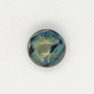 May include: A round, green, blue, and black glass marble with a swirling pattern.