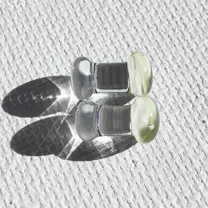 May include: Two clear glass ear gauges with a light yellow tint. The gauges are cylindrical with rounded ends.