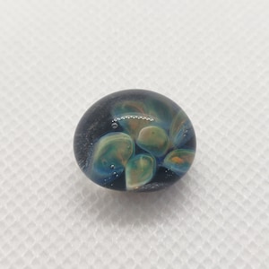 May include: A round glass paperweight with a dark blue background and swirling patterns of green, yellow, and orange.