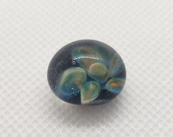 May include: A round glass paperweight with a dark blue background and swirling patterns of green, yellow, and orange.