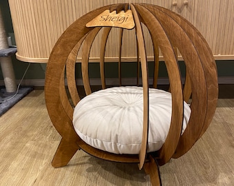 May include: A wooden cat bed shaped like a sphere with a round cushion inside. The bed has a nameplate on top that says "Sheigi".