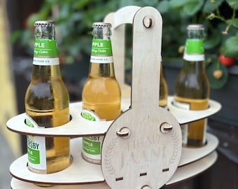 Könnte beinhalten: Holz-Sechserträger mit dem Text "Head Jaani 2024" auf der Unterseite. Vier Glasflaschen mit Apfelwein befinden sich im Träger.