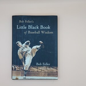 May include: A book titled "Bob Feller's Little Black Book of Baseball Wisdom" with a photo of Bob Feller pitching on the cover. The book is written by Bob Feller with Burton Rocks.