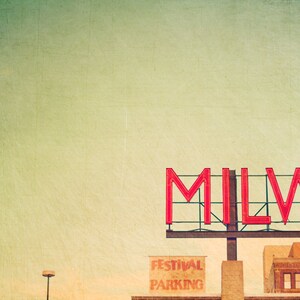 Könnte beinhalten: Ein Vintage-Bild eines roten Neon-Schilds mit der Aufschrift "MILWAUKEE" vor einem verblassten grünen Hintergrund. Unter dem Schild befindet sich ein kleineres Schild mit der Aufschrift "FESTIVAL PARKING".
