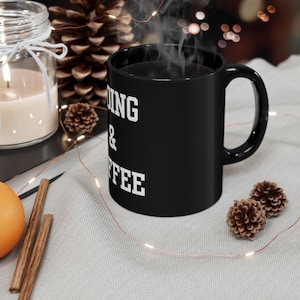 Könnte beinhalten: Schwarze Kaffeetasse mit weißem Text, der "Reading & Coffee" lautet. Die Tasse ist mit Kaffee gefüllt und Dampf steigt aus der Tasse auf.