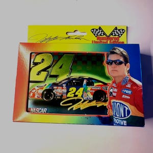 May include: A rectangular box featuring a NASCAR race car with the number 24, a portrait of a driver wearing sunglasses, and the text "Numberd Limited Edition" with checkered flags. The packaging includes a signature and vibrant rainbow-colored borders.