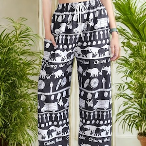 May include: Black and white patterned pants with an elastic waistband and drawstring. The pants feature a repeating pattern of elephants, vehicles, and text that says "Chiang Mai". The pants have pockets.