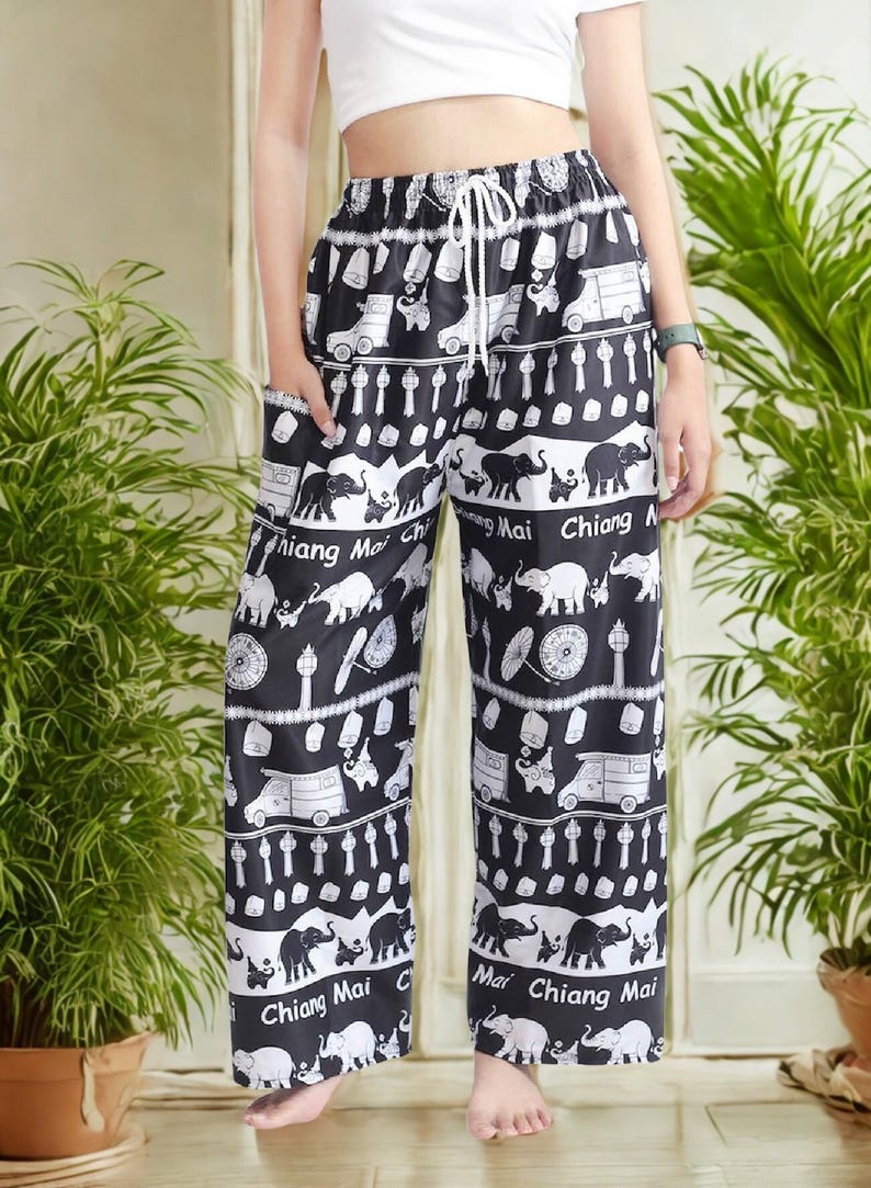May include: Black and white patterned pants with an elastic waistband and drawstring. The pants feature a repeating pattern of elephants, vehicles, and text that says "Chiang Mai". The pants have pockets.