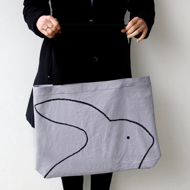 May include: A light gray tote bag with black fabric handles. The bag has a black silhouette of a rabbit printed on the front.