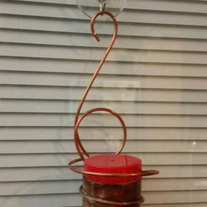 May include: A copper hummingbird feeder with a red top, hanging from a suction cup on a window.