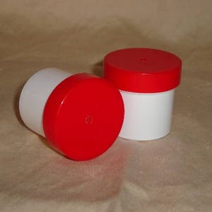 May include: Two white plastic containers with red lids. The containers are round and have a smooth surface.