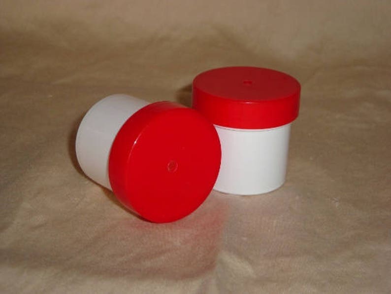 May include: Two white plastic containers with red lids. The containers are round and have a smooth surface.