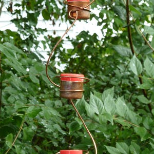 Pode incluir: Uma escultura de arame de cobre com tr&ecirc;s casti&ccedil;ais vermelhos e de cobre pendurados em um galho de &aacute;rvore.