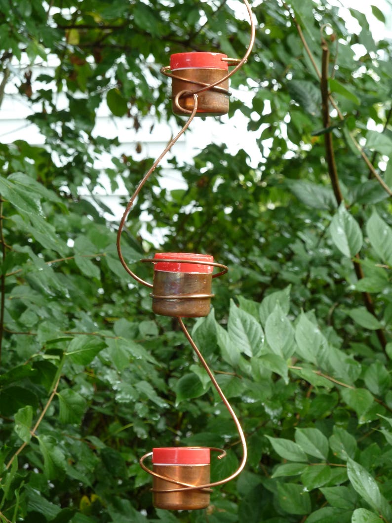 Pode incluir: Uma escultura de arame de cobre com tr&ecirc;s casti&ccedil;ais vermelhos e de cobre pendurados em um galho de &aacute;rvore.