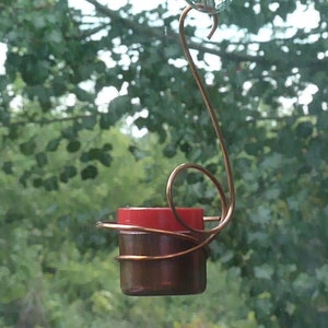 May include: A copper wire hummingbird feeder with a red glass base hanging from a window.