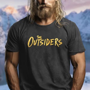 May include: A black t-shirt with a gold graphic of the text "THE OUTSIDERS" in a stylized font.
