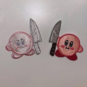May include: Two pink and red embroidered patches of a cartoon character holding a knife. The character has a round body, large eyes, and a small mouth. The knives are gray and white.