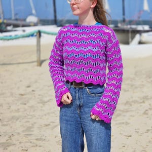 May include: A purple and blue crocheted sweater with a scalloped hem and bell sleeves.