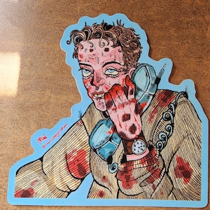 Könnte beinhalten: Ein Aufkleber mit einer Illustration einer verstörten Person, die einen Vintage-Telefonhörer hält. Das Gesicht und die Hand der Person sind mit rotem Blut bedeckt. Der Aufkleber hat einen hellblauen Rand und die Initialen "MW".