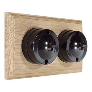May include: A pair of black toggle light switches mounted on a wooden plate. The switches have a vintage style and are made of black bakelite.