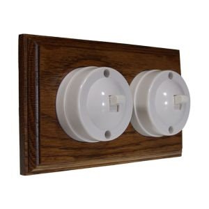May include: Two white porcelain light switches mounted on a dark wood plate. The switches have a round shape and a toggle switch.