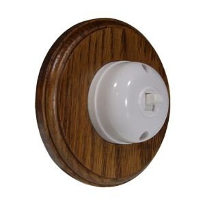 May include: A white ceramic light switch with a round wooden surround. The switch is mounted on a wall.