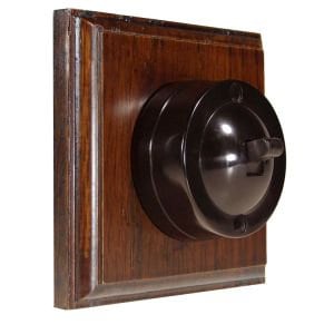 May include: A black bakelite light switch with a wooden surround. The switch is round and has a toggle lever.
