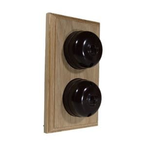 May include: A wooden wall plate with two black rotary light switches. The switches have a vintage style and are mounted on a light brown wooden plate.