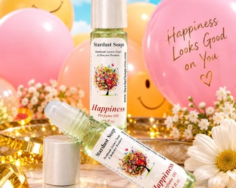 May include: Two clear glass perfume oil roller bottles with silver caps. The labels feature a colorful tree illustration and the text Stardust Soaps, Happiness Perfume Oil, and .33 fl. oz. The bottles are positioned among balloons and flowers.