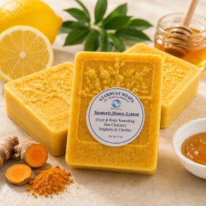 Puede incluir: Tres barras de jabón rectangulares amarillas con un diseño floral texturizado. Una etiqueta circular dice Stardust Soaps, Turmeric, Honey, Lemon, Face & Body Nourishing Skin Cleanser, Brightens & Clarifies, Net wt. 4 oz. Hay rodajas de limón, raíz de cúrcuma y miel presentes.