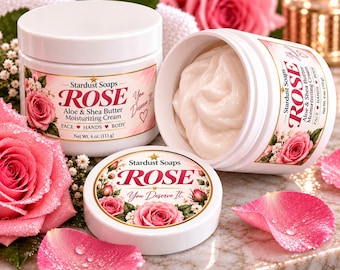 Könnte beinhalten: Zwei weiße Kunststofftiegel mit Stardust Soaps Rose Aloe & Shea Butter Feuchtigkeitscreme, einer geschlossen und einer offen mit weißer Creme. Die Etiketten zeigen rosa Rosen und den Text: Stardust Soaps ROSE You Deserve It, 113 g.
