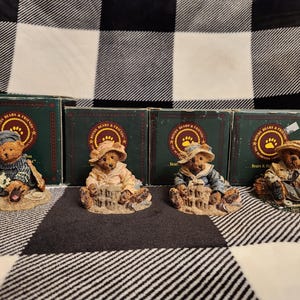 May include: Four small, hand-painted bear figurines, each in a different pose and wearing different clothing. The bears are sitting on small bases with the words "Boyds Bears & Friends" printed on the bases.