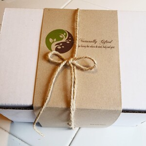 A white gift box is wrapped with a brown paper band featuring a green and brown yin-yang logo and the text "Naturally Gifted spa luxury that relaxes the mind, body and spirit," tied with twine.