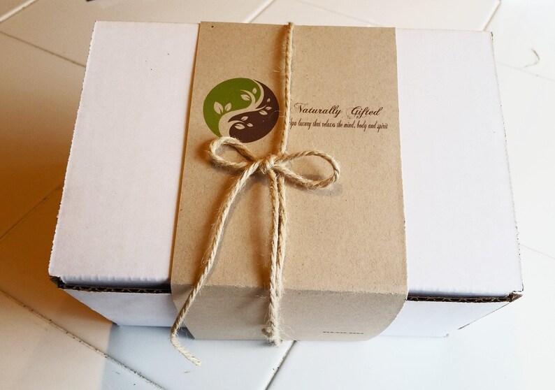 A white gift box is wrapped with a brown paper band featuring a green and brown yin-yang logo and the text "Naturally Gifted spa luxury that relaxes the mind, body and spirit," tied with twine.