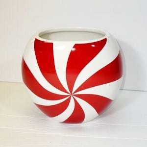 Pode incluir: Uma tigela redonda de cer&acirc;mica branca com um design espiral vermelho e branco. A tigela tem uma abertura larga e um acabamento brilhante. As listras vermelhas s&atilde;o espa&ccedil;adas uniformemente, criando um padr&atilde;o atraente. Esta tigela decorativa &eacute; adequada para v&aacute;rios usos.