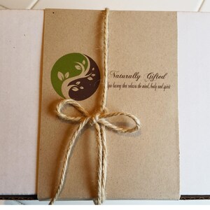 A white gift box is wrapped with a brown paper band featuring a green and brown yin-yang logo and the text "Naturally Gifted spa luxury that relaxes the mind, body and spirit," tied with twine.