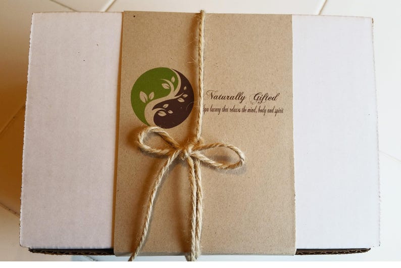 A white gift box is wrapped with a brown paper band featuring a green and brown yin-yang logo and the text "Naturally Gifted spa luxury that relaxes the mind, body and spirit," tied with twine.