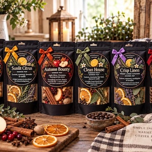 May include: Six black stand-up pouches containing dried fruit, spices, and herbs for simmer pots. Each pouch features a circular label with a unique scent name, including Country Cottage, Sunlit Citrus, Autumn Bounty, Clean House, Crisp Linen, and Sunday Bliss, tied with a small colored ribbon.