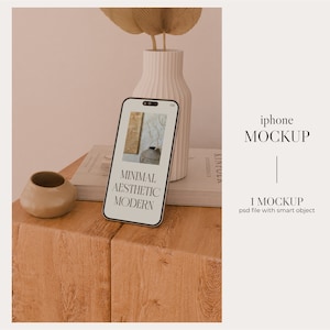 May include: A white iPhone mockup on a wooden surface with a book and a small vase with dried branches. The phone screen displays the text "Minimal Aesthetic Modern".