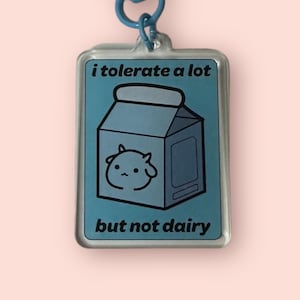 Peut inclure: Un porte-clés bleu avec un charme en plastique transparent qui dit "i tolerate a lot but not dairy". Le charme présente une illustration de dessin animé d'un carton de lait avec un visage de vache.