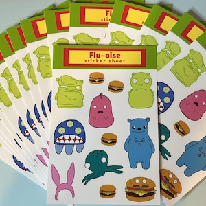 May include: A stack of sticker sheets featuring colorful cartoon monsters, burgers, and the text "Flu-oise sticker sheet." The stickers are in various shapes and colors, including green, blue, pink, and orange. The sheets have a green and red border.