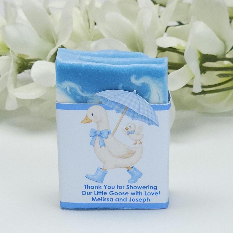 Blue silly goose baby shower soap favor featuring a handmade blue and white soap bar with a blue goose design label, personalized baby shower favor styled with white floral accents in the background