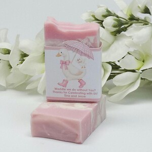 Pink silly goose baby shower soap favor displayed with one wrapped handmade pink soap bar featuring a goose design label and one unwrapped soap, styled with white floral accents in the background