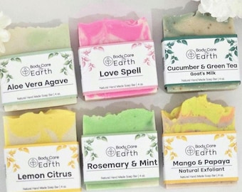 May include: Six bars of natural handmade soap with different scents and colors. The soaps are labeled with the names "Aloe Vera Agave", "Love Spell", "Cucumber & Green Tea Goat's Milk", "Lemon Citrus", "Rosemary & Mint", and "Mango & Papaya Natural Exfoliant".