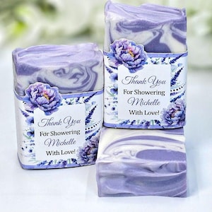Könnte beinhalten: Drei Seifenstücke in Lavendelfarbe mit Marmormuster. Jedes ist in eine dekorative Hülle mit floralem Muster und dem Text "Thank You For Showering Michelle With Love!" verpackt. Ein einzelnes, unverpacktes Stück ist ebenfalls zu sehen.