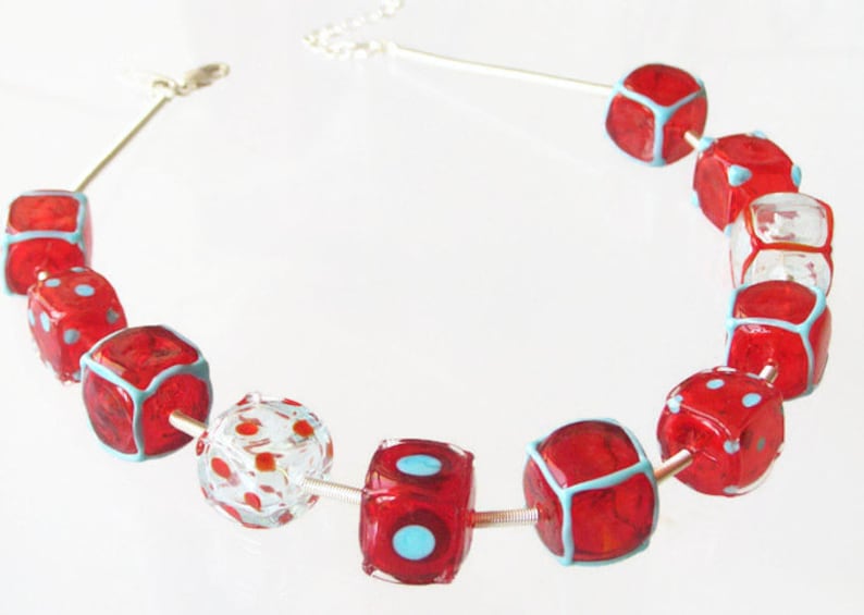 May include: A red and blue glass bead necklace with dice-shaped beads. The beads are red with blue outlines and white dots.