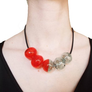 May include: A black cord necklace with alternating red and clear glass beads. The beads are round and have a slightly irregular shape.