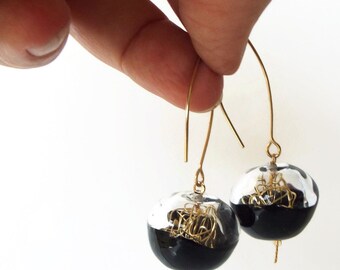 May include: A pair of gold dangle earrings with black and silver glass spheres. Each sphere contains a gold wire design.